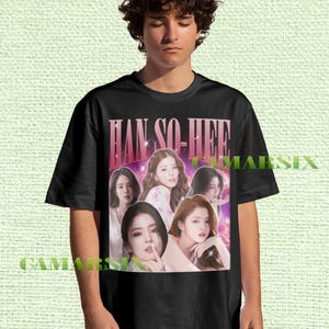 Könnte beinhalten: Schwarzes T-Shirt mit einem Retro-Grafik von Han So-hee. Das Design zeigt den Text "HAN SO-HEE" in einem rosa-violetten Farbverlauf. Das T-Shirt hat einen Rundhalsausschnitt und kurze Ärmel.