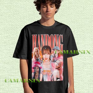 May include: Black t-shirt featuring a graphic of a group of people with the name "HANDONG" in a red, retro font. The graphic includes multiple images of the people in various poses and outfits. The shirt is worn by a person.