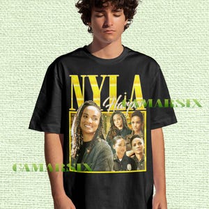 May include: Black t-shirt featuring a portrait of a woman with the name "NYLA Harper" in yellow block letters. The design includes multiple images of the same woman in various poses, framed in a yellow rectangle.