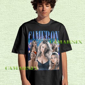 May include: Black t-shirt featuring a graphic of Cameron Diaz with her name in a blue and white font. The design includes multiple images of the actress. The shirt is worn by a person.