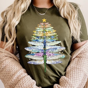 Può includere: T-shirt verde oliva con un design a forma di albero di Natale realizzato con ali di libellula multicolori. L'albero è sormontato da una stella dorata. Il testo "HEATHER OLIVE" è in basso.