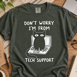 May include: A dark grey short-sleeve t-shirt featuring a white graphic of a black cat sitting on an open laptop. The text above the cat reads "DON'T WORRY I'M FROM TECH SUPPORT" and the text below the cat reads "TECH SUPPORT".