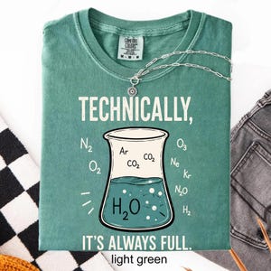 May include: A light green t-shirt featuring a graphic of a laboratory beaker filled with liquid. The text reads "TECHNICALLY, IT'S ALWAYS FULL." Chemical formulas including H2O, N2, O2, Ar, CO2, O3, Ne, Kr, N2O, and H2 are printed around the beaker.