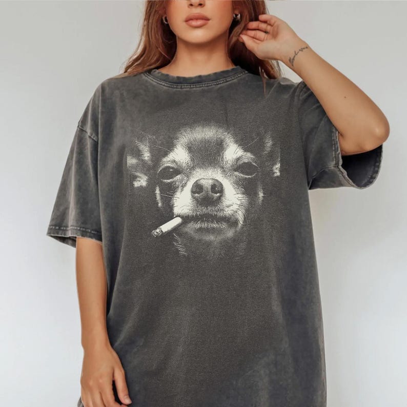 May include: Dark grey t-shirt with a black and white image of a Chihuahua smoking a cigarette. The tee has a vintage, worn appearance and a loose fit.