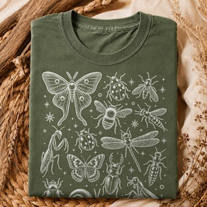 Puede incluir: Una camiseta de cuello redondo color verde oliva con un estampado gráfico de líneas blancas de varios insectos, incluyendo una polilla grande, una libélula, abejas, escarabajos y una mantis religiosa, intercalados con pequeñas estrellas.