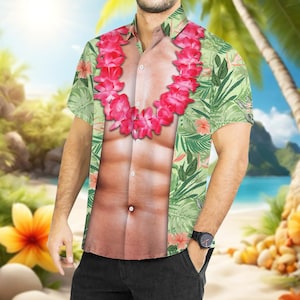 May include: Short-sleeved button-down shirt with a tropical floral print in shades of green, pink, and white. The shirt features a printed image of a muscular torso and a pink flower lei. A black watch is visible on the wrist.