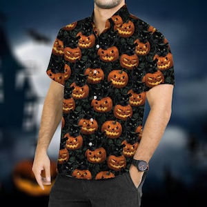 Puede incluir: Camisa de manga corta con temática de Halloween. La camisa presenta un patrón repetido de calabazas naranjas y gatos negros sobre un fondo verde oscuro. La camisa tiene un cuello clásico y la lleva una persona.