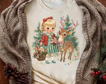 Op de afbeelding: Crèmekleurig T-shirt met een vintage illustratie van een meisje en een hert, een kerstboom en een mand met cadeaus. Het meisje draagt een rode strik, jasje en gestreepte jurk. Het hert heeft geweien versierd met lichtjes.