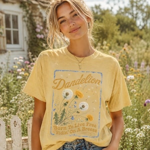 May include: Yellow t-shirt with a dandelion graphic. The graphic includes the word "Dandelion" in a script font, along with illustrations of dandelions and the text "Born To Live Free Ridin' On A Breeze."