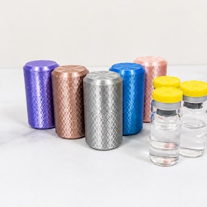May include: A collection of cylindrical metal caps featuring a diamond-patterned knurled texture in purple, copper, silver, blue, and pink, positioned alongside two small clear glass vials with yellow plastic caps and silver metal seals.