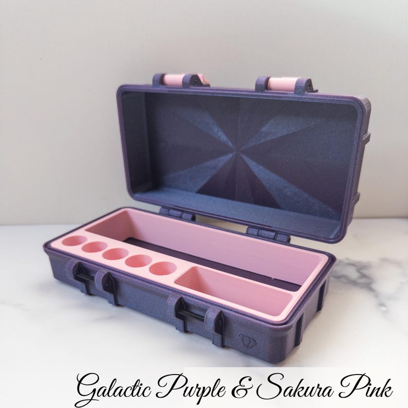 May include: Open purple and pink storage case with a geometric design on the inside of the lid. The interior features several circular compartments and a rectangular section. The text "Galactic Purple & Sakura Pink" is at the bottom.