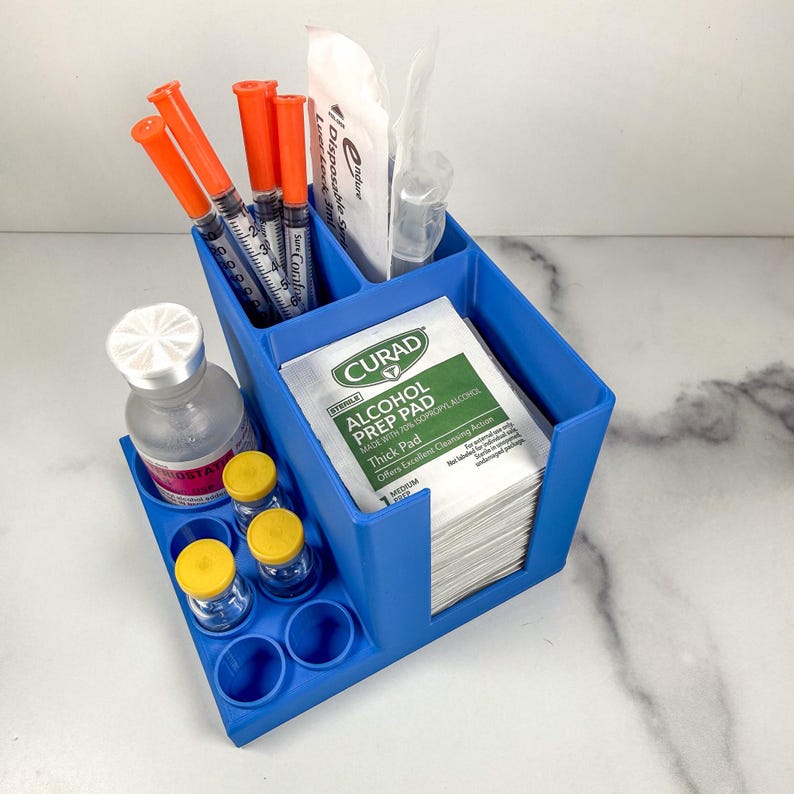 May include: A blue plastic organizer with multiple compartments. It holds syringes with orange caps, alcohol prep pads, vials, and other medical supplies. The organizer is designed to keep medical items neatly arranged and accessible.