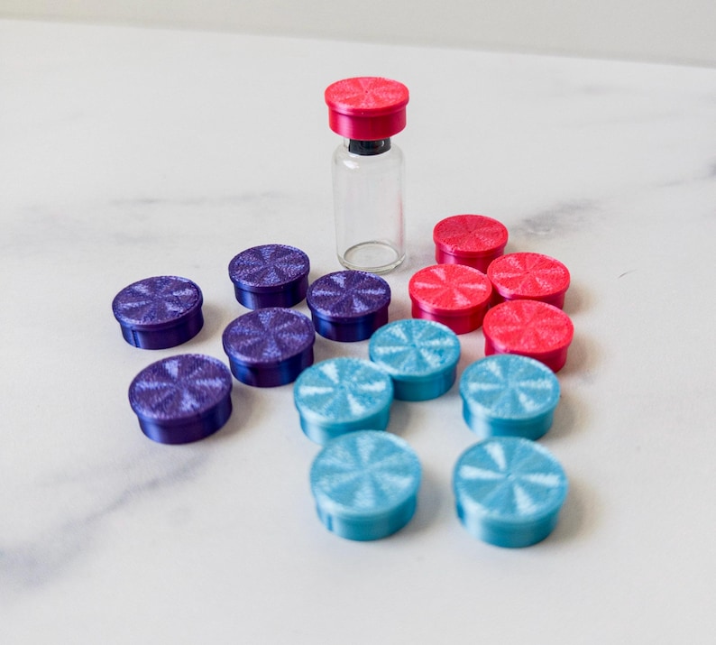 May include: A collection of colorful bottle caps in blue, purple, and pink. The caps have a starburst design and are arranged in a circle around a clear glass bottle.