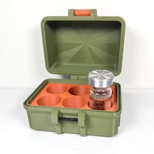 May include: An olive green hard-shell storage case with an orange latch and hinge. The interior features a bright orange foam insert with five circular cutouts, one of which holds a small clear glass vial with a metallic silver screw-top lid.