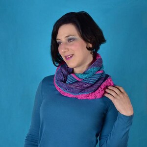 May include: A woman wearing a teal blue long-sleeved shirt with a pink and blue knitted scarf around her neck.