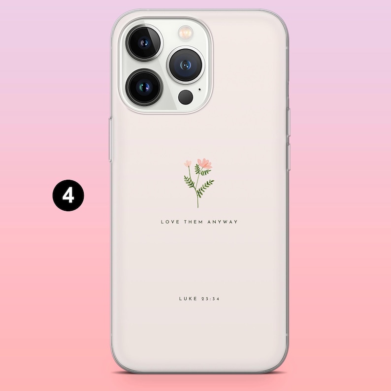 Pode incluir: Capa de telefone transparente com um design floral e o texto "LOVE THEM ANYWAY" e "LUKE 23:34". O design apresenta uma pequena flor rosa com folhas verdes. A capa &eacute; mostrada em um fundo gradiente rosa e branco.