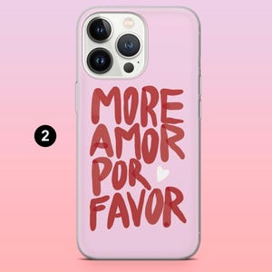 Puede incluir: Una funda de tel&eacute;fono rosa con la frase "MORE AMOR POR FAVOR" en rojo, con letras manuscritas. Un peque&ntilde;o coraz&oacute;n blanco est&aacute; entre "POR" y "FAVOR". La funda tiene un borde transparente y un c&iacute;rculo negro con el n&uacute;mero 2.