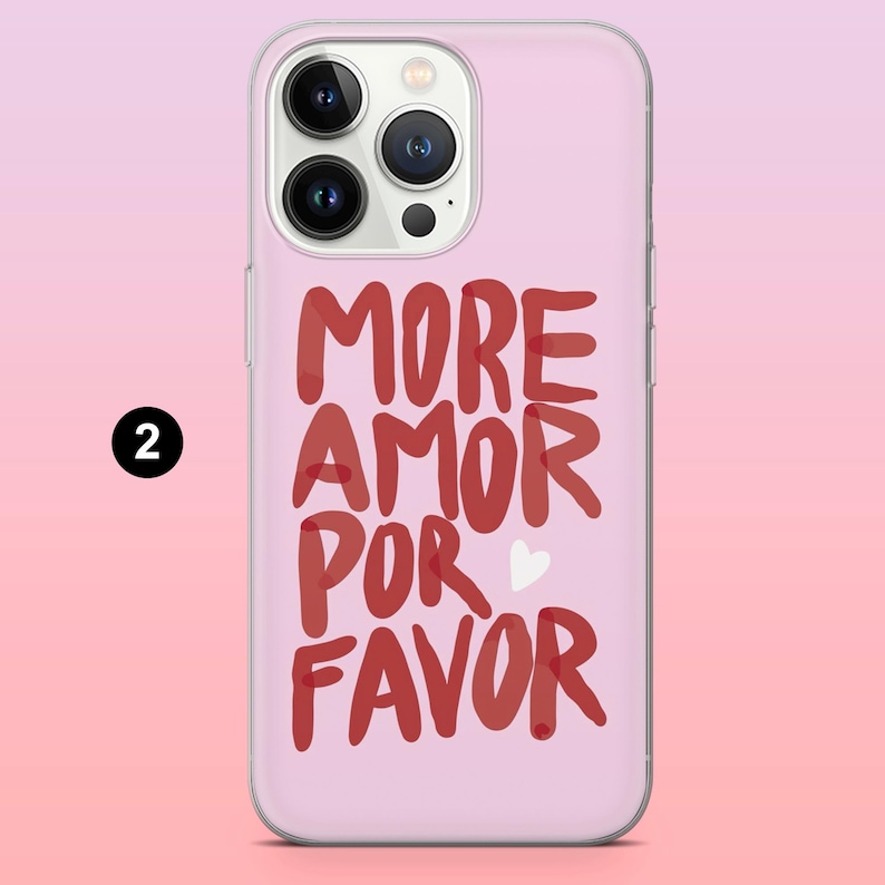 Puede incluir: Una funda de tel&eacute;fono rosa con la frase "MORE AMOR POR FAVOR" en rojo, con letras manuscritas. Un peque&ntilde;o coraz&oacute;n blanco est&aacute; entre "POR" y "FAVOR". La funda tiene un borde transparente y un c&iacute;rculo negro con el n&uacute;mero 2.