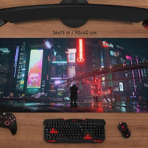 May include: A gaming mouse mat with a neon-lit cityscape design, measuring 90x40 cm. The mat features a futuristic urban scene with a person in a coat. A black keyboard, mouse, and controller are visible.