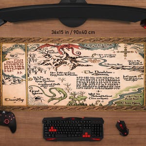 Puede incluir: Una alfombrilla de escritorio rectangular grande con un diseño de mapa, que mide 90 x 40 cm. El mapa presenta un dragón, montañas y texto. Se ven un teclado, un ratón y un controlador negros.