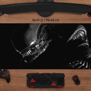 Puede incluir: Alfombrilla de ratón con temática Alien en blanco y negro, de 90x40 cm. El diseño presenta una imagen detallada de una criatura Alien. La alfombrilla está rodeada por un teclado, un ratón y otros accesorios de juego.