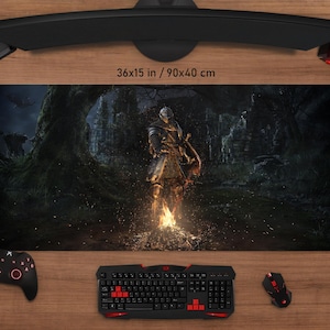 May include: A large gaming mouse pad, 36 x 15 inches, featuring a fantasy warrior in a dark forest setting. The pad has a black background with a detailed illustration and the text "36x15 in / 90x40 cm".