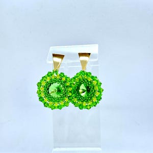 Könnte beinhalten: Ein Paar grüne und goldene Perlenohrringe mit einem klaren Kristall in der Mitte.