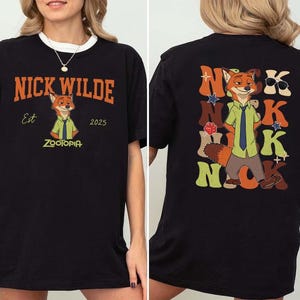 Peut inclure: T-shirt noir avec un motif de Nick Wilde de Zootopie. Le devant affiche le texte "Nick Wilde" en orange, l'illustration du personnage et "Est 2025 Zootopia". Le dos pr&eacute;sente un motif plus grand de Nick Wilde avec le mot "Nick" en plusieurs couleurs.