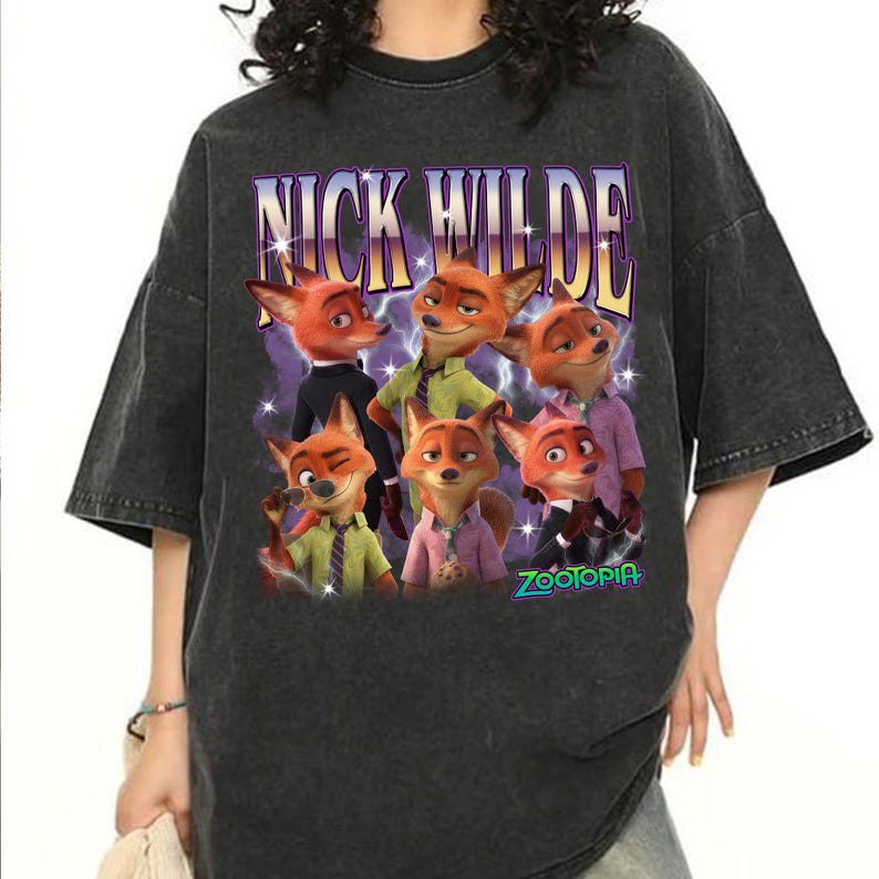 Puede incluir: Camiseta gris oscuro con un gr&aacute;fico de Nick Wilde de Zootopia. El dise&ntilde;o incluye m&uacute;ltiples im&aacute;genes del personaje zorro con el texto "NICK WILDE" en una fuente p&uacute;rpura y amarilla. La palabra "ZOOTOPIA" tambi&eacute;n es visible.