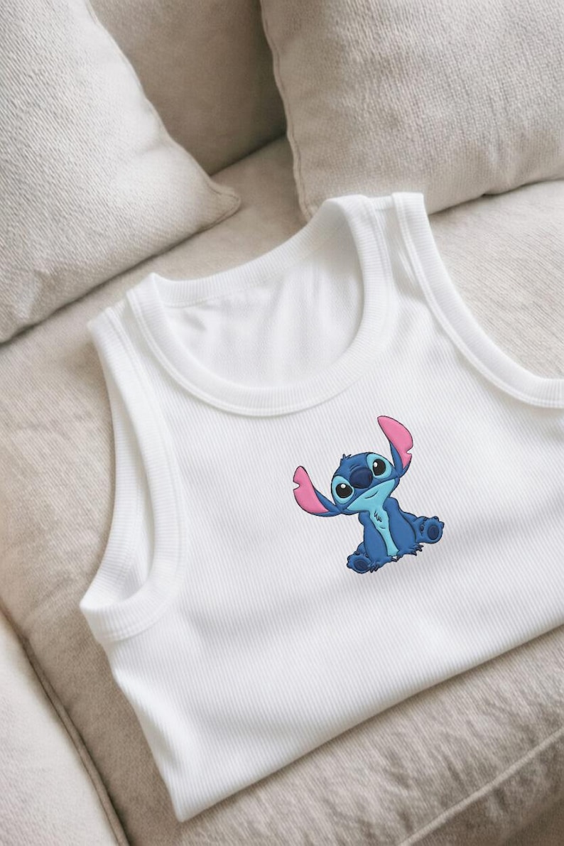 Puede incluir: Camiseta sin mangas blanca con dise&ntilde;o de personaje de dibujos animados azul. El personaje tiene orejas grandes y est&aacute; sentado con los brazos levantados. La camiseta sin mangas es de material suave y acanalado, adecuada para uso casual.