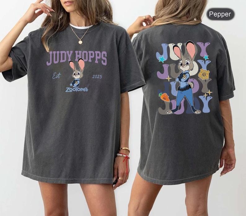 Peut inclure: T-shirt gris fonc&eacute; avec Judy Hopps de Zootopia. Le devant du t-shirt porte l'inscription "JUDY HOPPS" au-dessus d'une image de Judy Hopps, avec "Est 2025" et "Zootopia" en dessous. Le dos du t-shirt pr&eacute;sente une image plus grande de Judy Hopps.