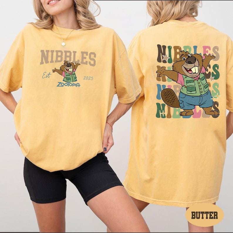 Peut inclure: T-shirt jaune avec un dessin de castor de dessin anim&eacute; et le mot "NIBBLES" en lettres marron. Le castor porte un gilet vert et un short bleu. Le dos du t-shirt pr&eacute;sente &eacute;galement le dessin du castor et le mot "NIBBLES".