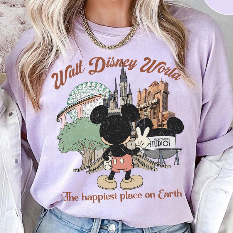 May include: A light purple sweatshirt featuring a graphic of Mickey Mouse with the text "Walt Disney World" and "The happiest place on Earth." The graphic includes images of the Epcot ball, a castle, and the Hollywood Tower Hotel.