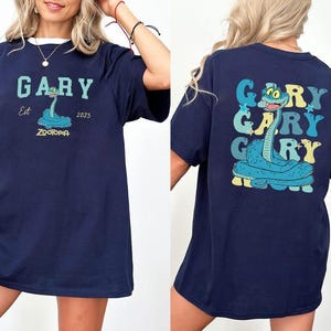 Peut inclure: T-shirt bleu marine avec un personnage de serpent de dessin anim&eacute; nomm&eacute; Gary de Zootopie. Le devant affiche "GARY" au-dessus du dessin du serpent, avec "Est 2025" et "ZOOTOPIA" en dessous. Le dos r&eacute;p&egrave;te "GARY" trois fois.