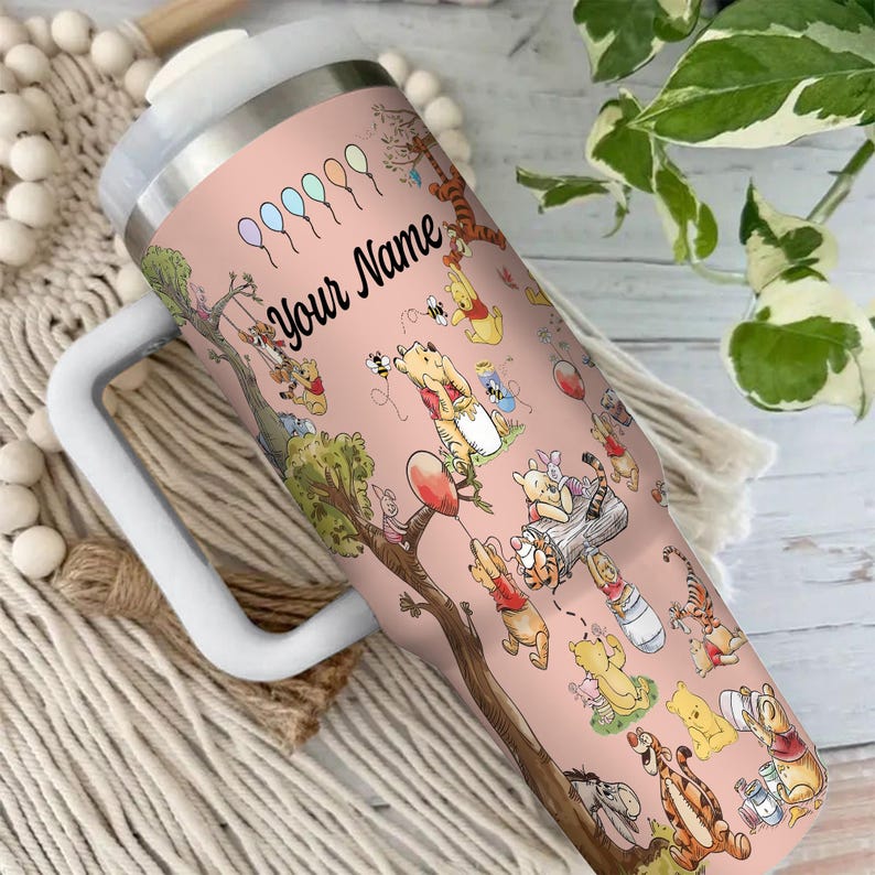 May include: A pink insulated tumbler featuring a whimsical design of Winnie the Pooh and friends. The tumbler has a white handle and lid, with the text "Your Name" in black script. The design includes balloons and various characters.