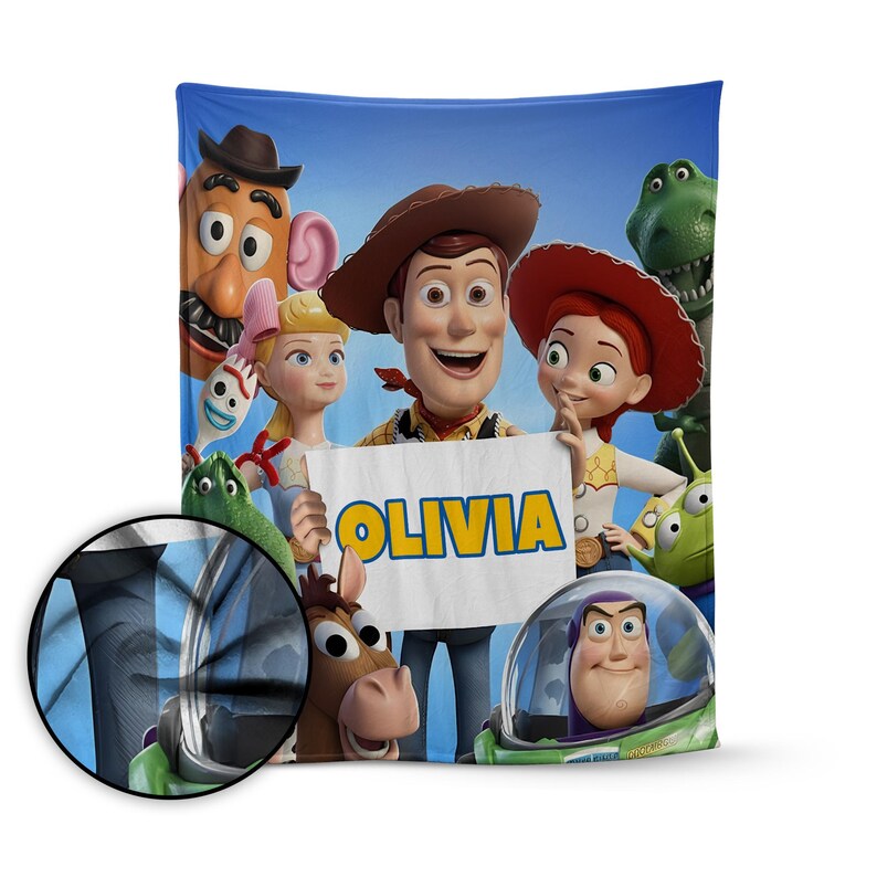 May include: A blue blanket featuring characters from the animated film Toy Story. The blanket includes Woody, Buzz Lightyear, Jessie, and other characters. The name "OLIVIA" is displayed on a sign held by the characters.