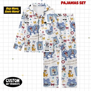 Puede incluir: Conjunto de pijama blanco con una camisa con botones y pantalones a juego. El conjunto presenta un patr&oacute;n repetido de personajes de Disney, lazos y elementos n&aacute;uticos en azul, rojo y amarillo. Las palabras "PAJAMAS SET" est&aacute;n impresas en la parte superior.