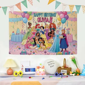 May include: A colorful birthday banner featuring various Disney princesses, balloons, and the text "HAPPY BIRTHDAY OLIVIA 5". The banner is decorated with confetti and streamers, creating a festive atmosphere. A birthday cake and other party decorations are in the foreground.