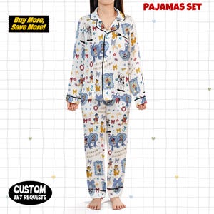 Puede incluir: Un conjunto de pijama blanco con estampado de personajes de dibujos animados, con una camisa con cuello abotonada y pantalones a juego. El conjunto tiene ribetes negros y el texto "PAJAMAS SET" es visible. La imagen tambi&eacute;n incluye el texto "Buy More, Save More!" y "CUSTOM ANY REQUESTS".