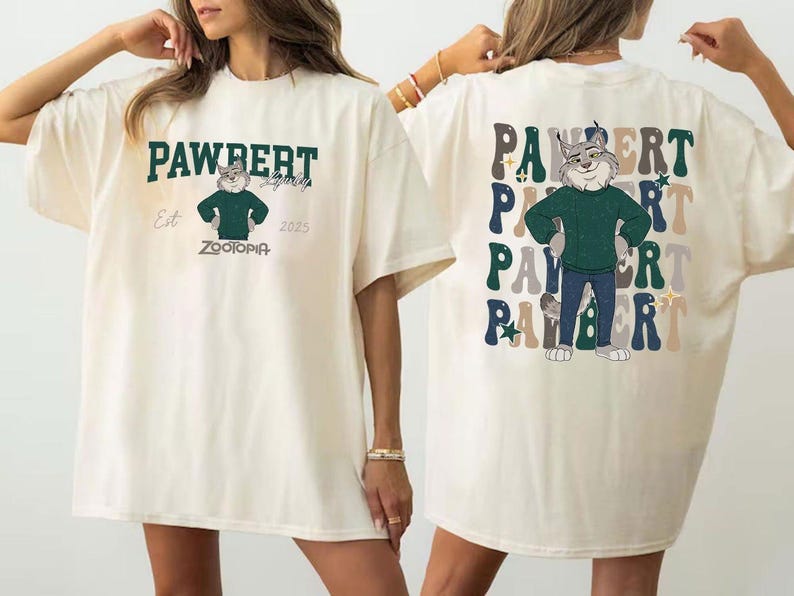 Peut inclure: T-shirt cr&egrave;me avec un personnage de dessin anim&eacute; de Zootopie. Le devant affiche le texte "PAWBERT" au-dessus du personnage, avec "Est 2025" et "ZOOTOPIA" en dessous. Le dos r&eacute;p&egrave;te "PAWBERT" avec le personnage au centre.