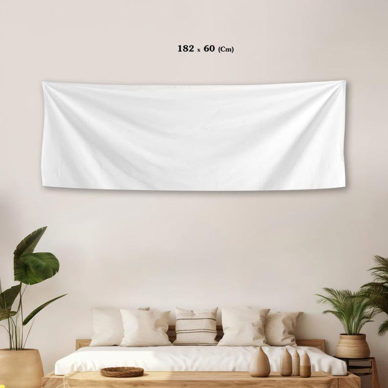 May include: A white rectangular wall tapestry, measuring 182 x 60 cm, hangs above a bed. The fabric is draped, creating soft folds. The room features plants and neutral-toned decor.