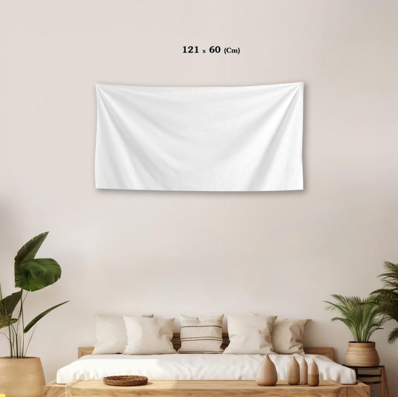 May include: A white rectangular wall tapestry, measuring 121 x 60 cm, hangs on a white wall. The fabric is slightly creased, suggesting a soft material. The tapestry is displayed above a bed with white pillows and a wooden frame.