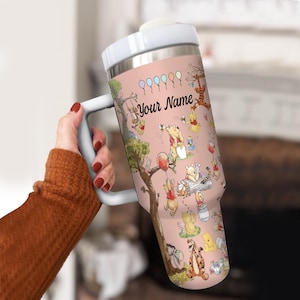 May include: A white ceramic mug with a black handle and the text "But First, Coffee" in a bold, black font. The mug is set against a blurred background, suggesting a cozy setting.
