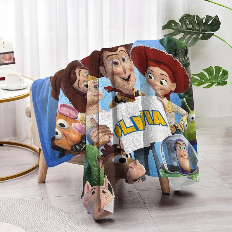 May include: A blue blanket featuring characters from the animated movie Toy Story. The blanket displays Woody, Jessie, Buzz Lightyear, and other characters. The name "OLIVIA" is printed on the blanket.