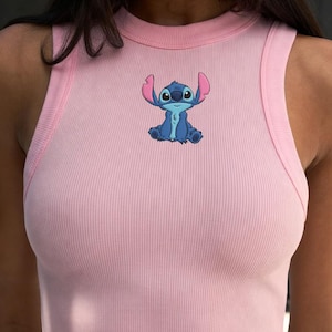 Puede incluir: Top corto rosa p&aacute;lido con costuras acanaladas y un personaje de dibujos animados azul. El top sin mangas tiene un cuello redondo y una silueta ajustada. El personaje est&aacute; en el centro.