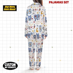 Puede incluir: Un conjunto de pijama blanco con un estampado repetido de personajes de dibujos animados, lazos y marcos. El conjunto incluye una parte superior de manga larga y pantalones, ambos con ribete negro. Las palabras "PAJAMAS SET" est&aacute;n impresas en la parte superior. Las palabras "Buy More, Save More!" est&aacute;n impresas a la izquierda.