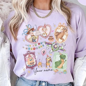 May include: A light purple long-sleeve shirt featuring cartoon characters from a popular animated movie. The design includes images of Woody, Buzz Lightyear, and other characters, with the text "Happy Birthday" and "Your name".