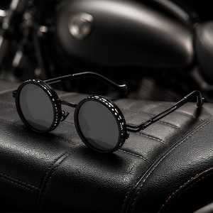 May include: Round sunglasses featuring a matte black metal frame with a distinctive side-shield design. The lenses are dark grey and circular, connected by a thin bridge. The temples are slender and black, matching the overall dark aesthetic.