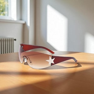 May include: Brown rimless sunglasses with a gradient lens. A white star is on the side of the frame. The sunglasses are on a wooden surface.