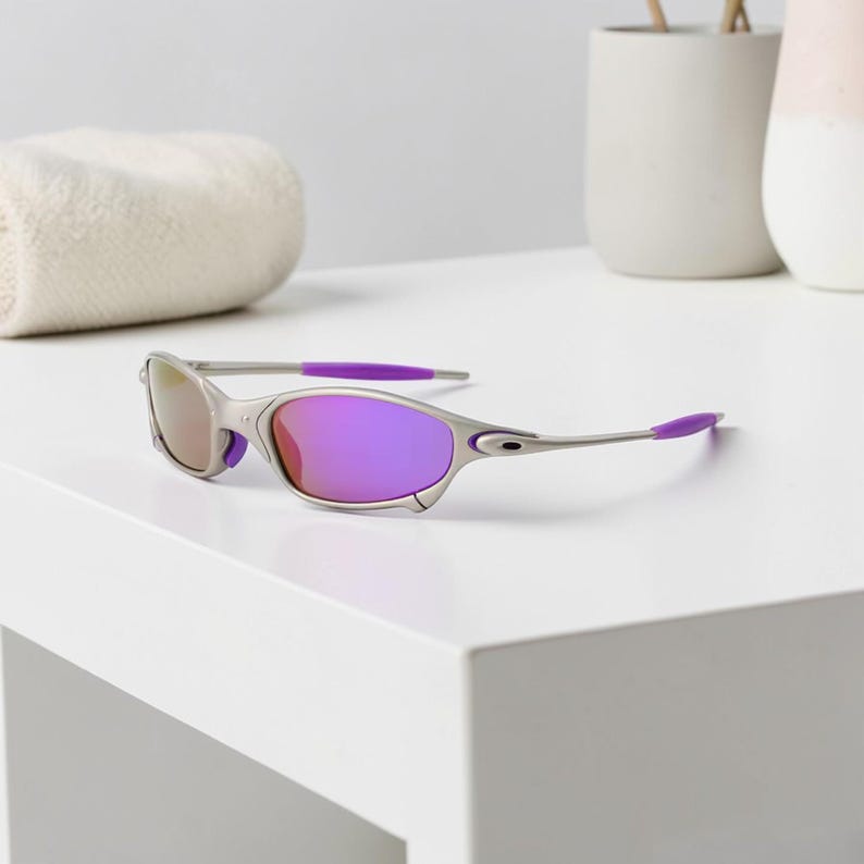 May include: Silver-framed sunglasses with purple lenses and accents. The sunglasses have a sleek, modern design with a curved frame and a pop of purple on the temples. The lenses reflect a gradient of colors.